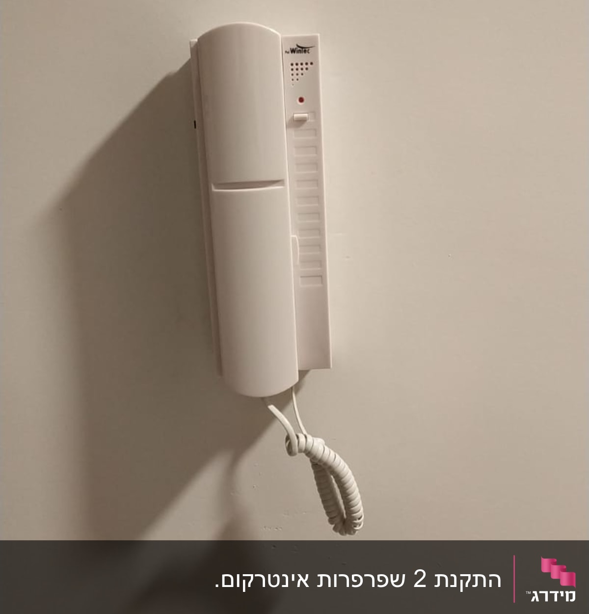 אינטרקום לבן תלוי על קיר עם שפופרת